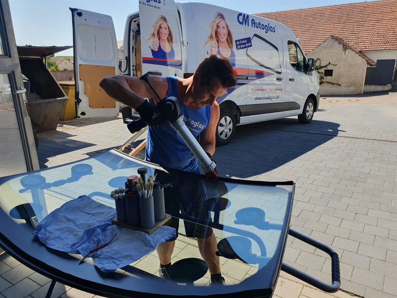 Monteur trägt mit der Kartuschenpistole eine Kleberaupe auf die neue Windschutzscheibe auf