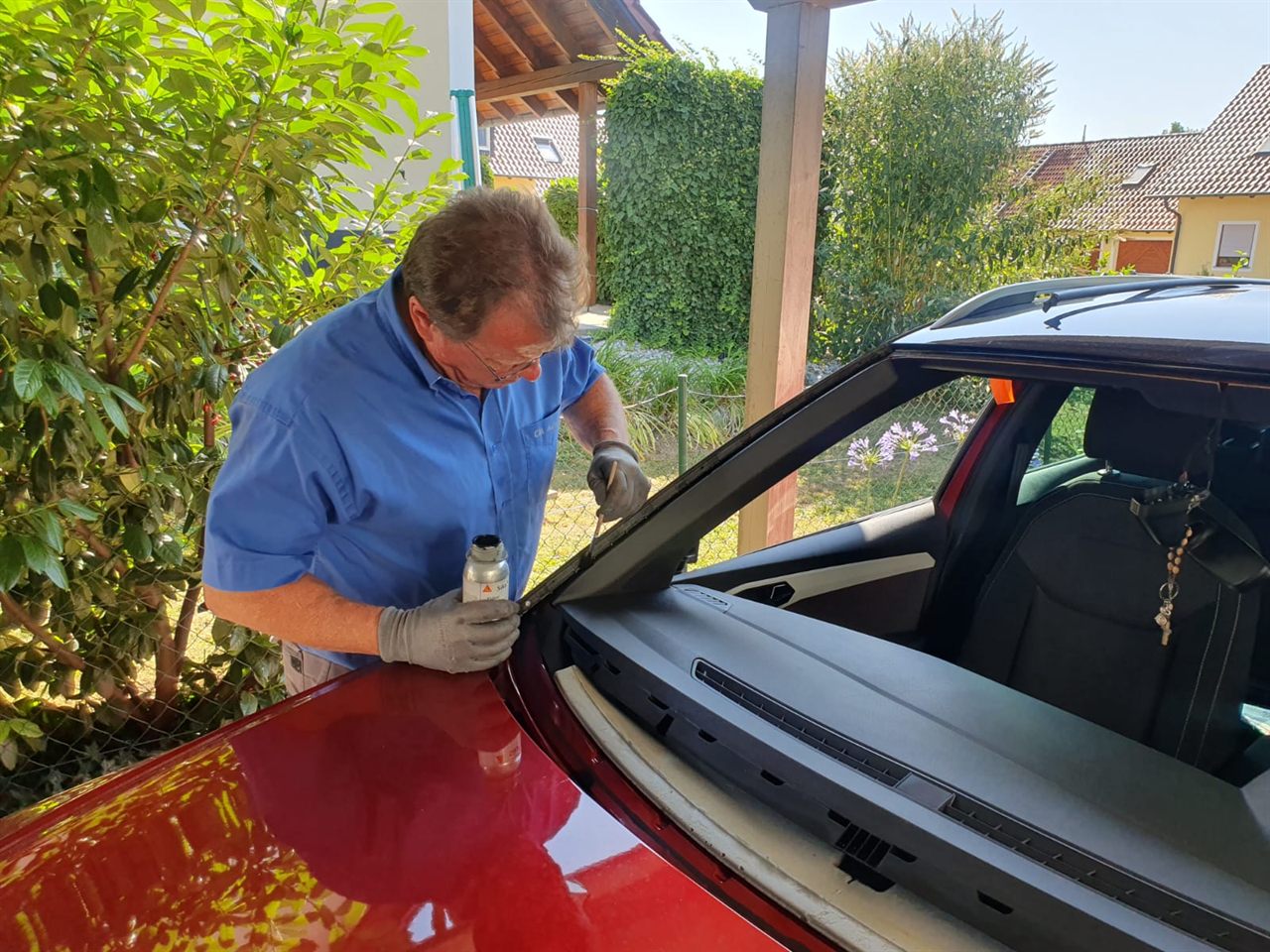 Monteur trägt Primer auf den Scheibenrahmen eines roten Fahrzeugs auf