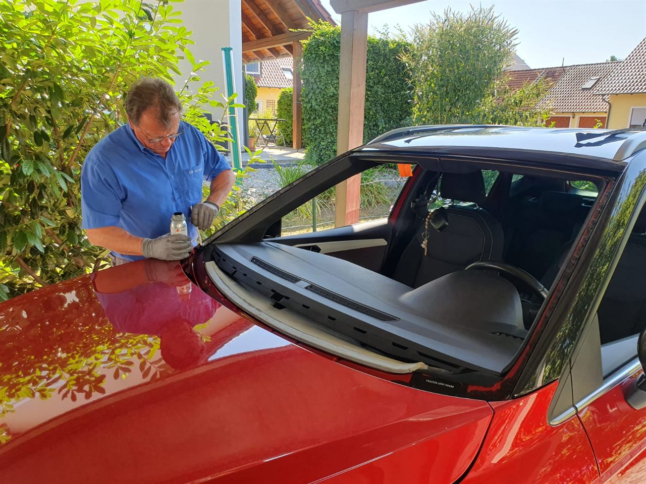 Monteur bereitet die Scheibenöffnung eines roten Fahrzeugs in einer Hofeinfahrt vor