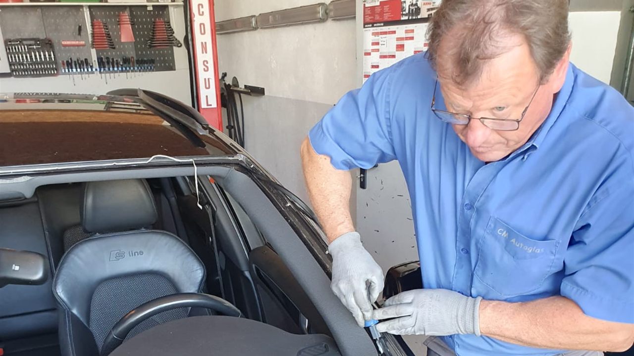Monteur von CM Autoglas arbeitet in der Werkstatt mit Handschuhen am Scheibenrahmen eines Fahrzeugs