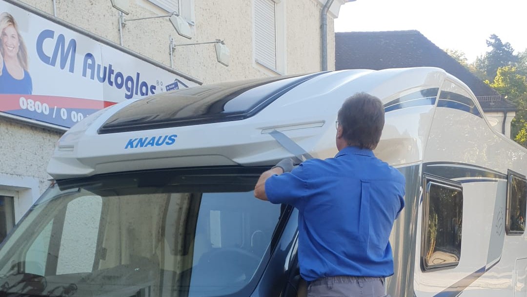 Monteur setzt auf einer Trittleiter die Frontscheibe eines Wohnmobils vor unserer Werkstatt in Deggendorf ein